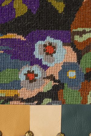 Close-up of embroidered flamingo textile with structured faux leather border and studs